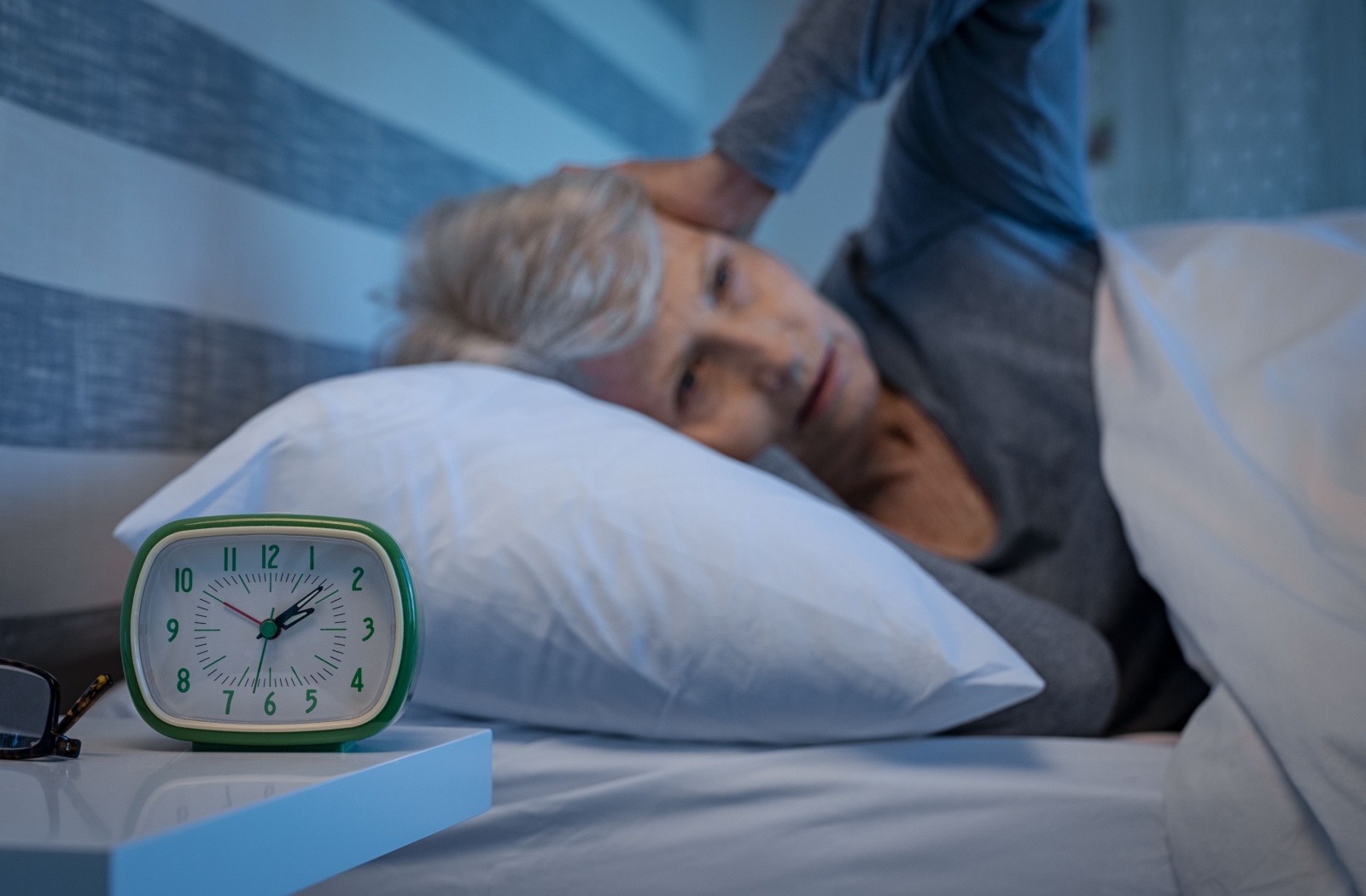 A senior struggles to fall asleep as an alarm clock reads just after 2am.