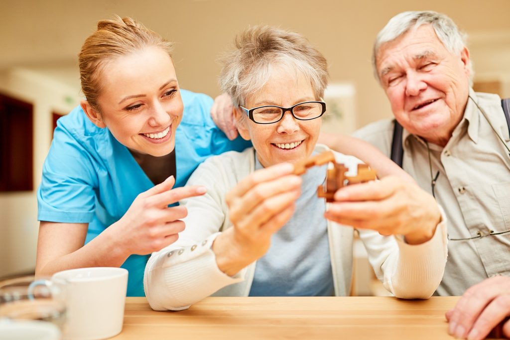 Smiling Female caregiver caring for and playing with happy seniors in a puzzle game with wooden puzzle